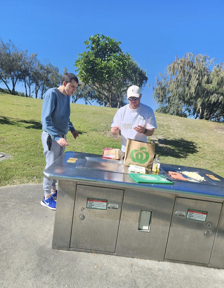 A support worker and participant cooking at a park barbecue