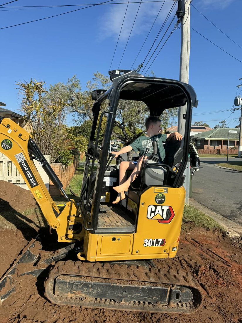A participant driving a mini excavator with support